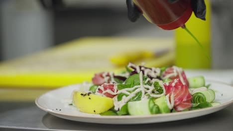 Close-up-of-a-cook-pouring-green-sauce-on-a-salad-before-serving-in-the-kitchen-in-a-restaurant.-The-cook-prepares-the-dishes-and-dresses-his-salad-before-serving-to-the-hall