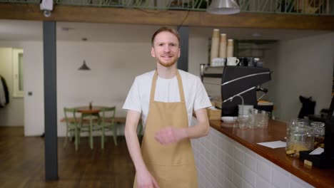 Portrait-of-a-happy-blond-guy-waiter-with-a-beard-who-crosses-his-arms-on-his-chest-and-poses-in-a-cafe