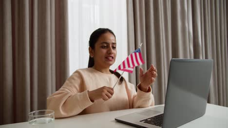 Happy-brunette-girl-in-light-pink-on-a-video-call-while-learning-English-at-home-online-in-a-modern-apartment.-Learning-foreign-languages-online-at-home