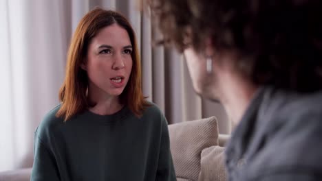 Over-the-shoulder-an-angry-brunette-girl-in-a-green-shirt-swears-with-her-boyfriend-while-talking-about-relationships-and-life-at-home-in-a-modern-apartment-on-the-sofa