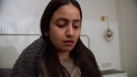 Portrait-of-a-sad-sick-brunette-girl-with-a-cold-in-a-brown-sweater-and-a-dark-gray-blanket-who-coughs-behind-her-hand-and-has-a-runny-nose-at-home-in-a-modern-apartment