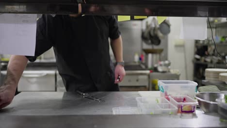 Close-up-of-a-confident-male-cook-in-a-black-shirt-arranging-containers-with-prepared-vegetables-before-starting-work-in-the-kitchen-in-a-modern-restaurant