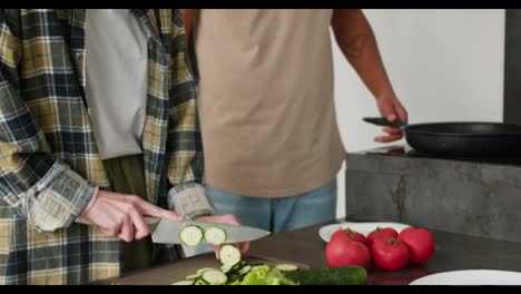 Close-up-a-young-adult-girl-with-brown-bob-hairstyle-prepares-a-salad-during-breakfast-and-feeds-chopped-vegetables-to-her-young-Black-brunette-boyfriend-in-the-kitchen-in-the-morning