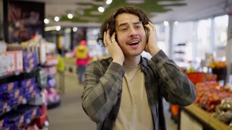 Happy-brunette-guy-with-curly-hair-and-headset-listens-to-cheerful-music-while-shopping-in-a-grocery-store