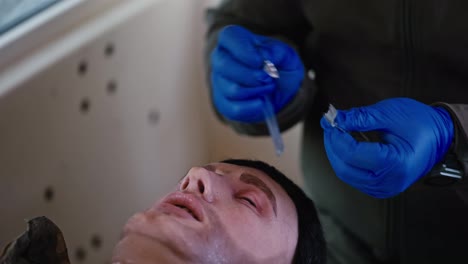 Un-Médico-Confiado-Con-Uniforme-Verde-Oscuro-Y-Guantes-Azules-Prepara-Un-Tubo-Para-Insertarlo-En-La-Nariz-De-Un-Muñeco-Soldado-Durante-El-Entrenamiento-Y-La-Realización-De-Un-Curso-De-Primeros-Auxilios-En-Condiciones-Militares