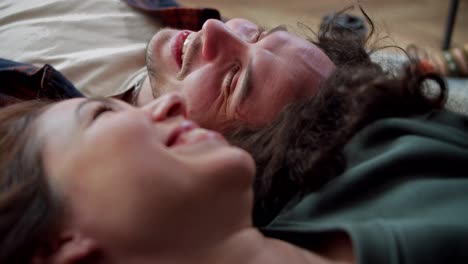 Close-up,-a-happy-brunette-guy-with-curly-hair-lies-on-the-floor-head-to-head-with-his-brunette-girlfriend-and-talks-and-laughs-at-home-in-a-modern-apartment