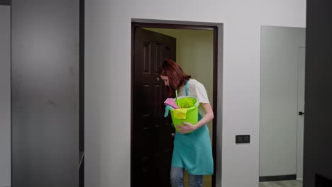 A-confident-trio-of-cleaners-in-blue-aprons-on-call-take-turns-entering-a-modern-apartment-carrying-in-their-hands-various-items-for-cleaning-the-apartment