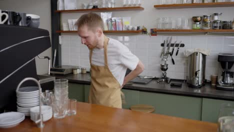 A-blond-barista-guy-in-a-yellow-apron-and-a-white-T-shirt-starts-his-day-and-work-behind-the-counter-in-a-cafe