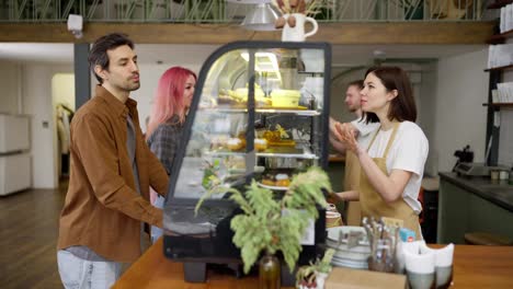 A-brunette-man-in-a-brown-jacket-chooses-a-cake-and-makes-his-order-while-chatting-with-a-brunette-girl-barista-in-a-cafe