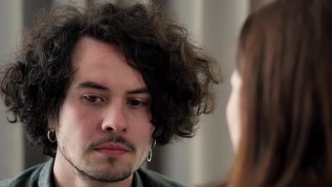 Over-his-shoulder-a-sad-brunette-guy-with-curly-hair-and-a-mustache-listens-to-a-brunette-girl-dissatisfaction-with-him-at-home