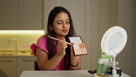 A-happy-brunette-girl-with-Brown-skin-shows-her-Beauty-blog-viewers-what-powder-she-uses-and-talks-about-cool-cosmetics-during-her-Beauty-blog-in-a-modern-apartment-at-home