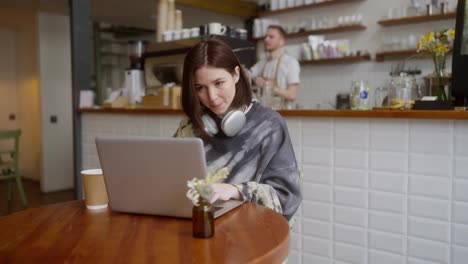 Close-up-of-a-confident-brunette-girl-concentrated-working-in-front-of-a-laptop-while-sitting-at-a-table-in-a-cafe