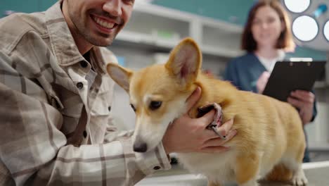 Portrait-of-a-happy-brunette-guy-in-a-plaid-shirt-posing-with-his-yellow-white-corgi-dog-in-the-veterinarian-office-at-a-veterinary-clinic