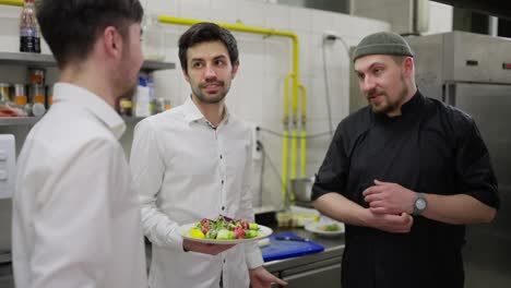 Communication-between-two-male-waiters-in-white-shirts-and-a-professional-cook-in-a-black-uniform-while-solving-professional-issues-in-the-kitchen-of-a-restaurant