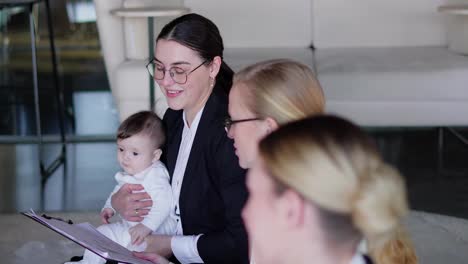 A-confident-brunette-girl-in-round-glasses-businesswoman-business-clothes-holds-a-small-infant-child-in-her-arms-during-her-businesswoman-meeting-on-the-carpet-during-a-break-between-work