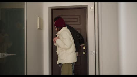 Happy-young-man-with-Black-skin-color-brunette-in-a-black-jacket-comes-home-with-his-young-adult-girlfriend-in-a-plaid-shirt-and-white-jacket-after-a-walk-in-a-modern-apartment