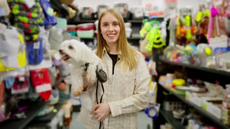 Portrait-of-a-happy-blonde-girl-in-a-checkered-light-shirt-with-her-white-cheerful-dog-in-a-pet-store.-Portrait-of-a-happy-girl-who-came-to-the-pet-store-with-her-dog