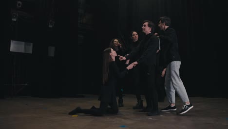 Confident-young-actors-in-black-suits-stand-on-stage-and-play-and-rehearse-their-roles-while-their-stage-director-expressively-tells-them-what-to-do-during-rehearsals-and-preparation-for-the-performance