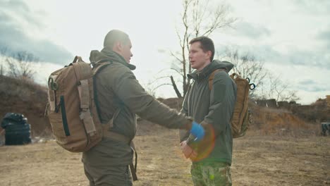 Side-view-of-a-confident-military-man-in-a-dark-green-uniform-and-with-a-backpack-on-his-shoulders-pats-his-colleague-and-partner-on-the-shoulder-as-a-sign-of-support-outside-the-city