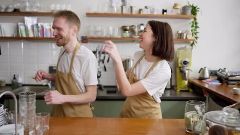 Ein-Glückliches-Brünettes-Mädchen-Tanzt-Synchron-Mit-Ihrem-Kellnerkollegen,-Während-Sie-An-Der-Bartheke-In-Einem-Café-Steht