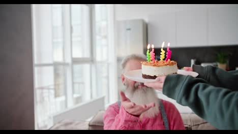 A-brunette-girl-in-a-green-jacket-brings-a-cake-along-with-candles-for-her-elderly-dad-with-gray-hair-and-a-lush-beard-for-his-birthday-in-a-modern-apartment