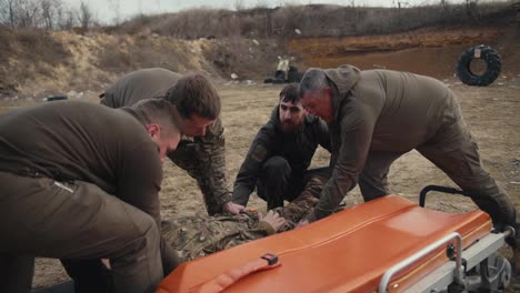 Four-confident-men-and-a-soldier-in-a-green-uniform-shift-a-training-doll-of-a-male-soldier-in-a-camouflage-uniform-onto-an-ambulance-worn-during-training-in-providing-medical-assistance-on-the-battlefield