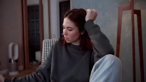 A-tired-brunette-girl-in-a-gray-jacket-drinks-tea-from-a-cup-and-thinks-about-life-while-sitting-in-a-cozy-room-in-a-modern-apartment