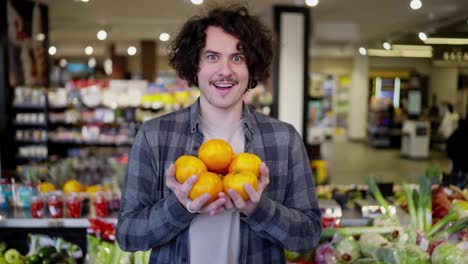 Portrait-of-a-happy-guy-with-curly-hair-in-a-plaid-shirt-holding-yellow-fruits-in-his-hands-in-a-supermarket-while-shopping-at-a-grocery-store