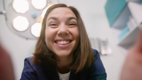 Portrait-first-person-view-of-a-happy-brunette-veterinarian-girl-in-a-blue-uniform-holds-a-pet-in-her-hands-during-an-examination-in-a-veterinary-clinic-and-smiles-broadly-at-it