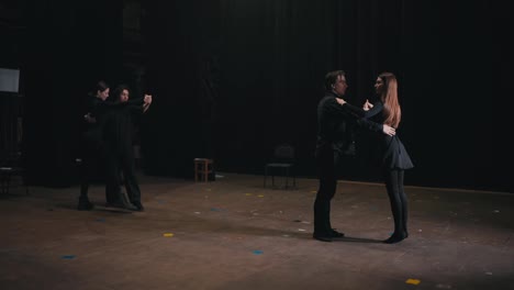 Two-pairs-of-actors-in-black-suits-dance-a-slow-dance-and-rehearse-their-act-on-stage-before-a-performance-in-the-theater.-Beautiful-slow-dance-as-the-finale-of-the-actors-performance-on-stage