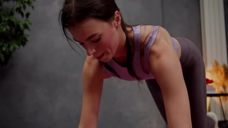 Close-up-shot-of-a-confident-athletic-brunette-girl-in-a-purple-top-running-on-the-spot-using-a-sports-mat-in-a-modern-apartment-at-home.-Confident-brunette-girl-feels-sweat-on-her-face-during-intense-exercise-at-home