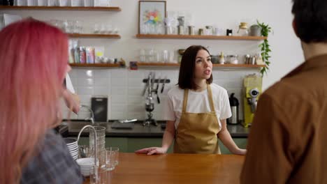 Over-the-shoulder-a-happy-couple-a-brunette-guy-and-a-girl-with-pink-hair-communicate-with-waiters-in-a-cafe-at-the-cash-register-and-place-their-order