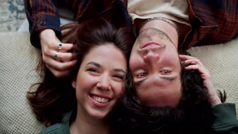 Portrait-of-a-happy-brunette-girl-and-a-guy-with-curly-hair-who-are-lying-head-to-head-on-pillows-at-home-and-smiling-in-a-modern-apartment