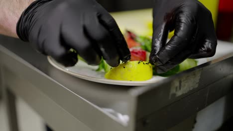 Close-up-shot-of-a-confident-male-cook-in-black-protective-rubber-gloves-placing-a-slice-of-lemon-on-a-dish-with-salad-Before-serving-in-a-restaurant