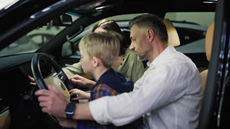 A-middle-aged-man-with-gray-hair-in-a-white-shirt-along-with-his-wife-and-little-blond-son-with-blue-eyes-are-sitting-in-the-interior-of-a-modern-car-during-their-trip-to-a-car-dealership