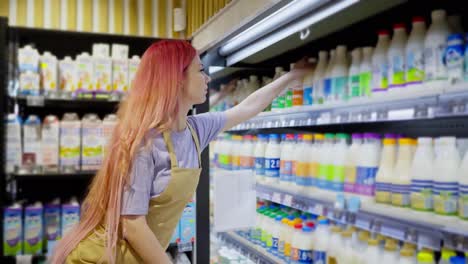 Side-view-of-a-girl-supermarket-worker-with-pink-hair-placing-goods-on-the-dairy-products-counter-in-a-supermarket