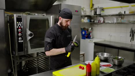 Confident-male-chef-in-a-black-uniform-with-a-black-bandana-and-gloves-peels-an-avocado-while-preparing-a-salad-in-the-kitchen-in-a-restaurant.-Confident-chef-with-beard-peels-vegetables-before-starting-to-prepare-salad-in-modern-kitchen