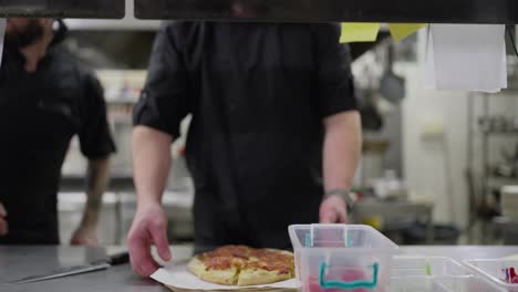 Un-Cocinero-Con-Uniforme-Negro-Pasa-Un-Plato-Para-Entregar-Desde-La-Cocina-Según-Un-Pedido-Específico-Mientras-Trabaja-En-Un-Restaurante.-Un-Chef-Profesional-Coloca-Un-Plato-En-Una-Mesa-De-Servicio-Para-Que-El-Camarero-Se-Lo-Entregue.