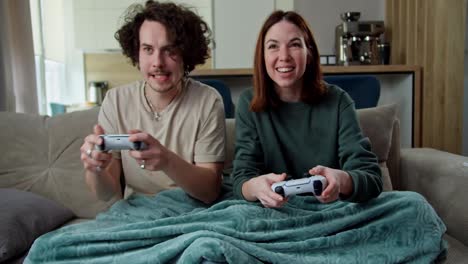 Happy-and-confident-brunette-guy-with-curly-hair-plays-with-a-joystick-with-his-girlfriend-who-beats-him-in-a-video-game-while-sitting-on-the-couch-at-home