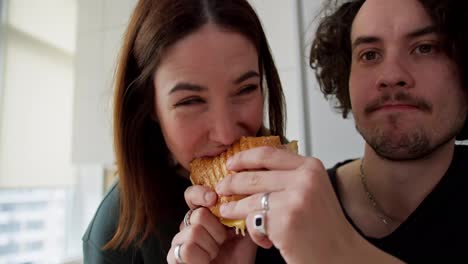 Una-Chica-Morena-Feliz-Muerde-Un-Sándwich-En-Las-Manos-De-Su-Novio-Que-Quería-Comer-Para-El-Desayuno-Por-La-Mañana-En-Un-Apartamento-Moderno-En-La-Cocina.