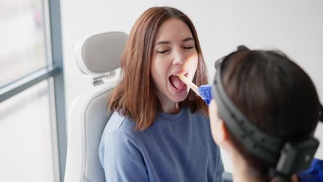 Over-the-shoulder-of-a-confident-girl-a-brunette-doctor-puts-a-special-stick-to-check-the-girls-throat-during-an-appointment-in-the-ENT-office-in-a-modern-clinic