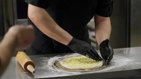 Close-up-a-professional-chef-in-black-clothes-with-black-gloves-carefully-prepares-pastries-and-arranges-a-cheese-cake-in-the-desired-shape-on-a-table-in-a-restaurant