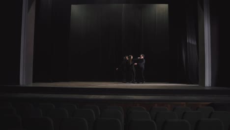 Side-view-of-a-group-of-confident-and-happy-actors-in-black-clothes-in-the-theater-going-on-stage-near-a-black-curtain-during-a-rehearsal-in-an-empty-hall