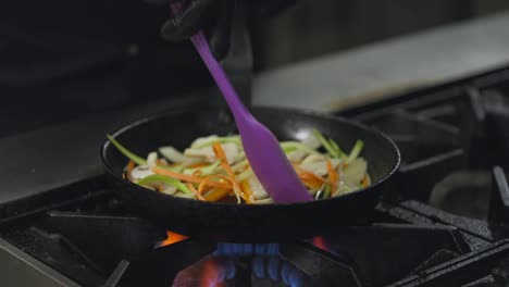 Close-up-a-professional-chef-stirs-chopped-thinly-sliced-vegetables-on-a-hot-frying-pan-on-a-gas-burner-while-preparing-a-dish-in-the-kitchen-of-a-restaurant