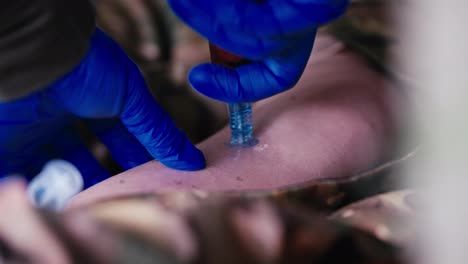 Close-up-a-confident-medic-inserts-a-needle-into-the-leg-with-his-hands-in-rubber-blue-gloves-to-introduce-a-special-medicine-into-the-body-of-a-wounded-soldier-in-camouflage-uniform-on-the-battlefield