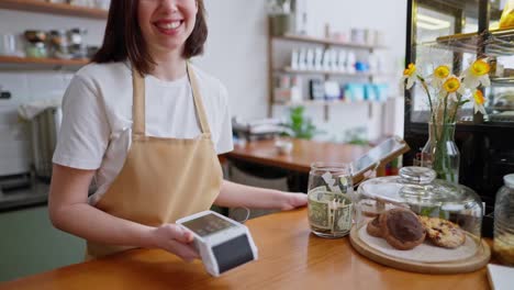 Primer-Plano:-Un-Cliente-De-Una-Cafetería-Paga-Un-Pedido-Usando-Un-Teléfono-Y-Una-Terminal-De-Barista-Y-Una-Niña-Agita-Su-Mano-En-Una-Cafetería.