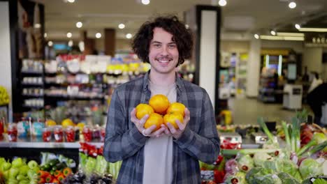 Portrait-of-a-happy-brunette-guy-with-a-mustache-holding-yellow-fruits-in-his-hands-and-posing-in-a-grocery-store