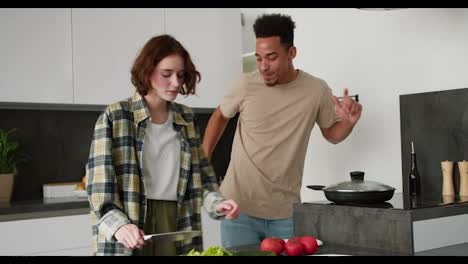 Happy-young-Black-brunette-man-in-a-cream-t-shirt-dances-with-his-young-adult-girlfriend-with-brown-hair-and-bob-hairstyle-while-they-are-preparing-breakfast-together-in-the-morning-in-a-modern-kitchen