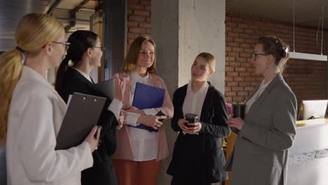 Side-view-of-a-group-of-confident-businesswomen-in-business-clothes-communicating-during-a-short-break-in-a-modern-office