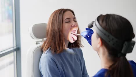 A-brunette-girl-opens-her-mouth-wide-while-a-brunette-girl.-The-ENT-doctor-puts-a-wand-and-looks-at-the-girls-throat-using-a-special-light-device-and-then-tells-her-good-news-in-a-modern-clinic